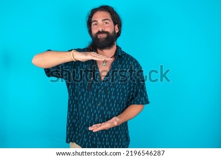 Caucasian man with beard wearing blue shirt over blue background gesturing with hands showing big and large size sign, measure symbol.
