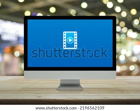 Play button with movie flat icon on desktop modern computer monitor screen on wooden table over blur light and shadow of shopping mall, Business cinema online concept