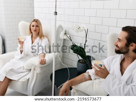 Couple in love during intravenous vitamin therapy. Beautiful woman with her boyfriend with glasses of refreshing drink with lemon in medical clinic for detox their organisms Royalty-Free Stock Photo #2196573677
