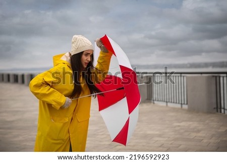 Woman in yellow raincoat with umbrella caught in gust of wind outdoors