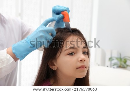 Doctor using nit comb and spray on little girl indoors. Anti lice treatment