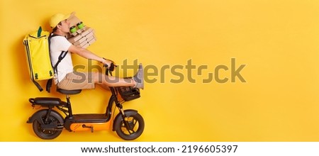 Portrait of funny scared delivery man in cap riding bicycle, having accident, holding pizza boxes and takeaway drink, wearing thermo backpack isolated over yellow background.