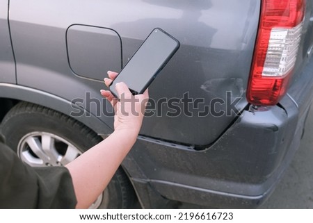 Woman takes a picture of damage to the bumper of her car on a smartphone. Insurance inspector examines the damage to the bumper. Royalty-Free Stock Photo #2196616723
