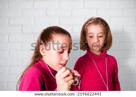 Couple of Little Girls Taking Picture Using Toy Photo Camera, white brick wall on background