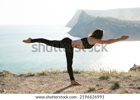 Meditation in a complex yoga pose, balancing on the edge of a cliff overlooking the sea at dawn Royalty-Free Stock Photo #2196626991