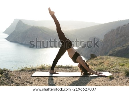 Meditation in a complex yoga pose on the edge of a cliff at sunset. Eka pada Adho mukha Shvanasana