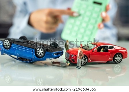 woman office worker sits at a table with a simulation of an accident of two cars. The concept of auto accident insurance. Life and health insurance during an accident