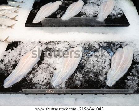The white fish fillet on the black tray in the crushed ice for sale in the supermarket, front view with the copy space.