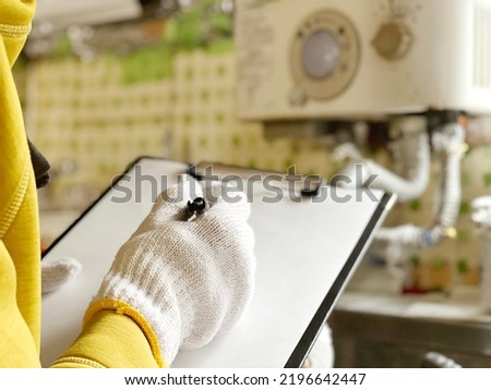 Gloved hands filling out a clipboard in front of an instant water heater Royalty-Free Stock Photo #2196642447