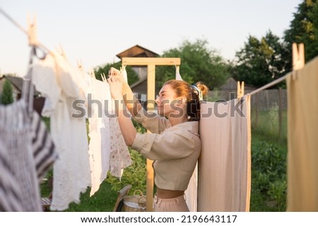 Laundry day. A woman hangs linen and towels on a tree in the courtyard of a village house. Summer cottage concept. Royalty-Free Stock Photo #2196643117