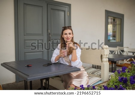 a young pretty girl drinks a non-alcoholic cocktail in a cafe on the veranda, a portrait of a girl in a street cafe with a drink in her hands. High quality photo