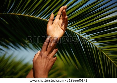 Hands skin care. Photo of African female hands with manicure against palm leaf's background. Natural beauty product concept