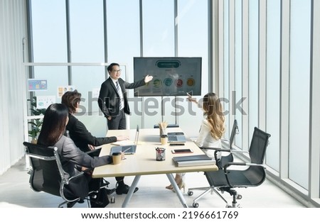 Asian business man presenting work on television screen with woman looking at computer laptop in office meeting room