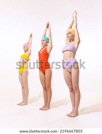Portrait of three young women in vintage retro swimming suits posing isolated over grey studio background. Exercises. Concept of beauty, fashion, vintage style, summertime, party. Copy space for ad Royalty-Free Stock Photo #2196667803