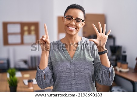 African american woman working at the office wearing glasses showing and pointing up with fingers number six while smiling confident and happy. 