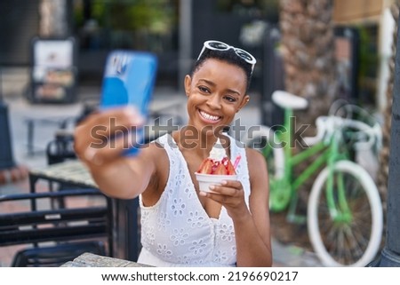 African american woman eating ice cream make selfie by smartphone at coffee shop terrace