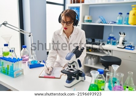 Young caucasian woman wearing scientist uniform listening to music working at laboratory