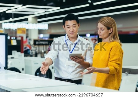 Asian consultant salesman in electronics and household appliances store, selling a working machine to a woman, recommending and approving the choice Royalty-Free Stock Photo #2196704657