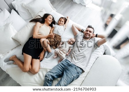 Young parents and their children lie in bed top view. Father, mother and their daughter and newborn son spend the day off at home and have fun in bed. Happy family enjoy spending time with each other Royalty-Free Stock Photo #2196706903