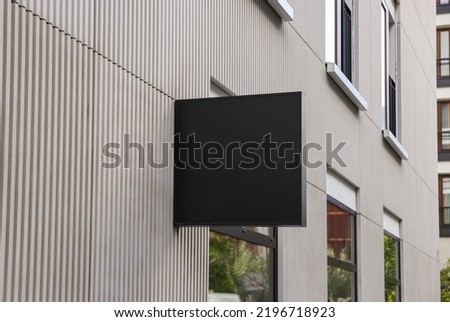 Empty square black street sign near the entrance to the building. Mockup, place to insert a logo or design