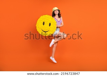 Full size photo of brunette funky lady jump with smile wear hat top shorts shoes isolated on orange color background