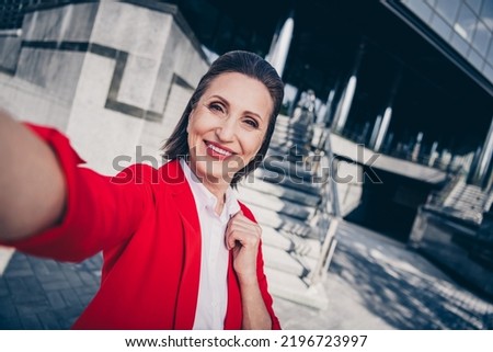 Photo of cheerful pretty cute senior clerk woman dressed red blazer recording self video outdoors urban town street