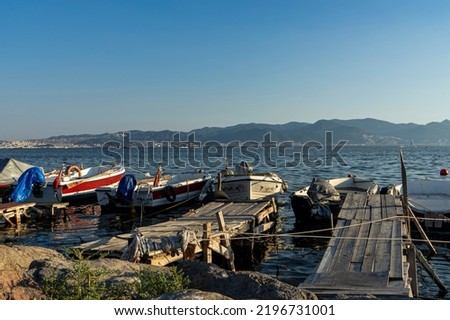 Small fishing boats moored to wooden piers in Karsiyaka, Mavisehir with beautiful Izmir city view on the background.