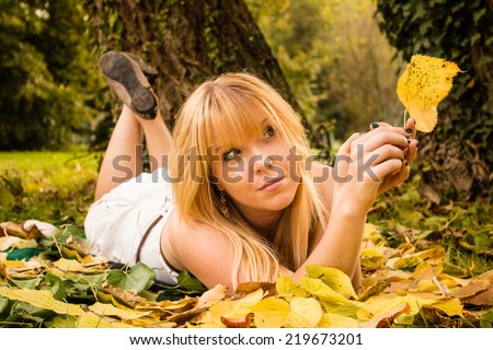 beautiful blonde girl relaxing lying down holding a yellow autumn leaf.