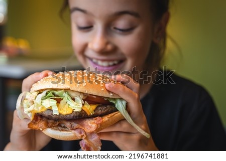 A little girl eats an appetizing burger, close-up. Royalty-Free Stock Photo #2196741881