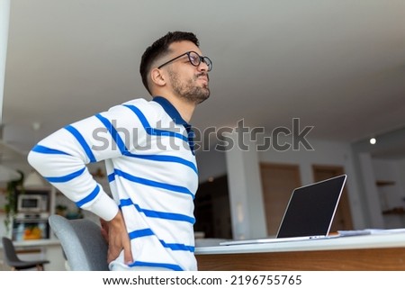 Shot of a young businessman suffering from a backache while working at his desk in his office.