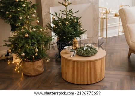 Several stylish Christmas trees stand in the living room by the marble fireplace