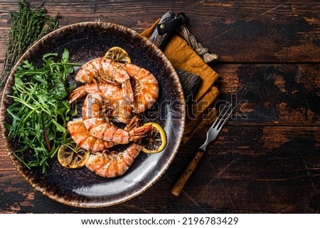 Spicy garlic Giant shrimps prawns in plate with salad. Wooden background. Top view. Free copy space.