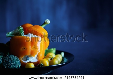 Colorful stuffed sweet orange bell pepper as monster with cut out face carved into a Halloween pumpkin Jack O'Lantern and filled with Tzatziki dip. Selective focus with blurred background. 