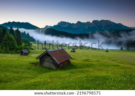 Small cabin on mountain meadow at forest edge, Geroldsee in the background Karwendel Mountains at sunrise, Kaltenbrunn, Upper Bavaria, Germany Royalty-Free Stock Photo #2196798575