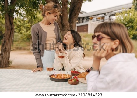 Three pretty young caucasian girls relax sitting at picnic table in park. Women wear casual clothes spring. Holiday life concept