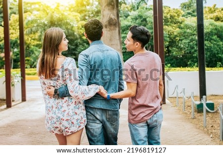 Unfaithful girl walking in the park with her boyfriend while holding another man hand. Love triangle concept. Woman holding hands with another man while walking with her boyfriend outdoor Royalty-Free Stock Photo #2196819127