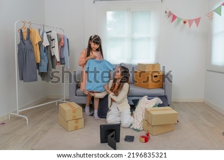 Mother and daughther as team working from home social live chat online sale business via computer tablet pc and show sample cloth and size meassurement before packing to the box and seal adhesive tape