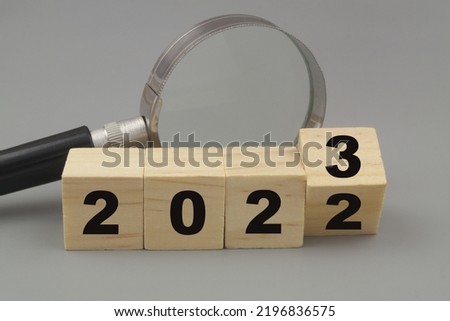 Prognosis and events in year 2023. Magnifying glass and wooden cubes with numbers 2023 and 2022 on gray background.