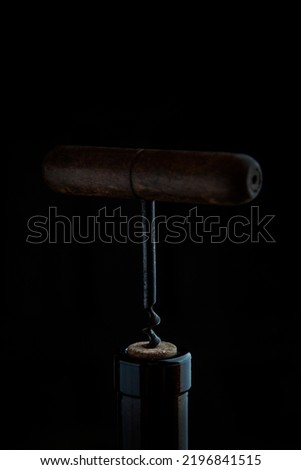 A bottle of wine opens with a corkscrew. A corkscrew with a wooden handle. Out of focus.Selective focus. Vertical photo on a dark background.