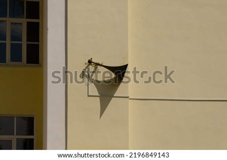 An old loudspeaker hangs on a yellow wall.