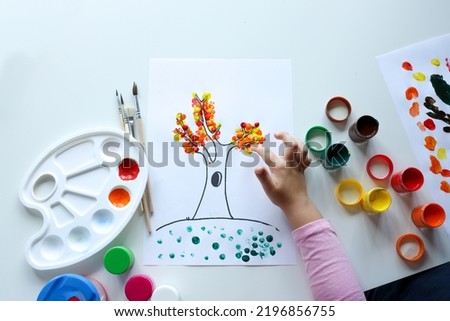 A child draws leafs on a tree. Ideas for drawing with finger paints. Finger painting for kids on white background. Little girl painting by finger hand paint color. Children development concept. Royalty-Free Stock Photo #2196856755