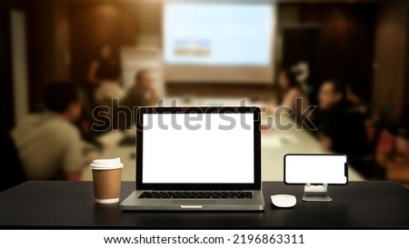 Front view of cup and laptop, smartphone, and tablet on black table in meeting room
