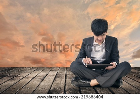 Asian business man using pad and sit on ground.