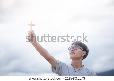 Young man in glasses holding christian lift up a cross for worshipping God. Concept religion. Focus on face. Copy space for your individual text.