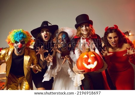 Group of young people dressed up as spooky characters having fun at Halloween costume party. Adult male and female friends with scary makeup on faces doing claw gesture, hissing and making grimaces Royalty-Free Stock Photo #2196918697