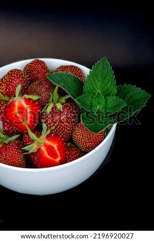 Large ripe strawberries with a fresh sprig of mint, on a black background, close-up