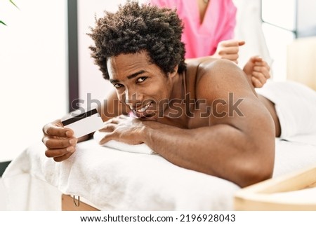 Young african american man having massage holding credit card at beauty center
