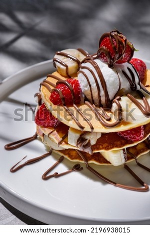 Pancakes with chocolate topping, strawberries, banana and ice cream in a plate on a concrete table