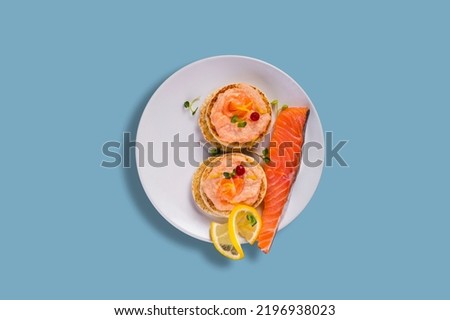 Sandwiches with salmon fillet, lemon, mung bean salad, red currant and caviar paste in a plate on a blue background