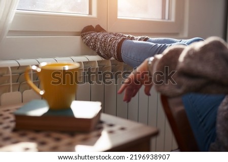 Woman heating feet on a chilly winter day, energy and gas crisis, cold room, heating problems. Royalty-Free Stock Photo #2196938907